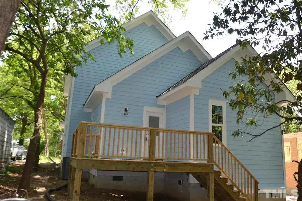 Light blue house with a wooden front porch and stairs under leafy trees