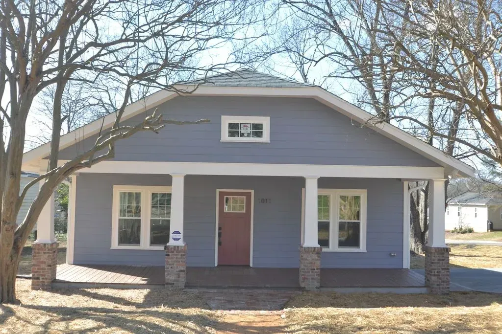 Small gray house with a front porch, red door, and white-trimmed windows under leafless trees