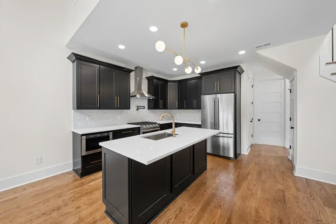 Modern kitchen with dark cabinets, white island, stainless steel refrigerator, and wood floors.