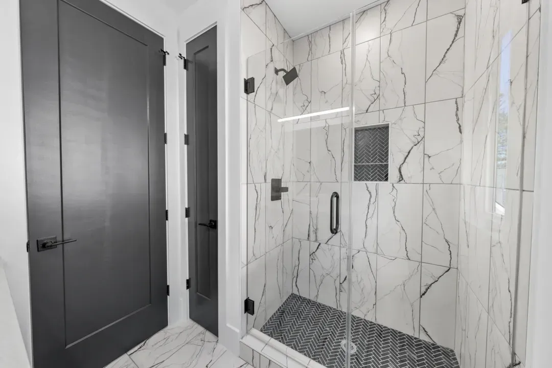 Modern bathroom with marble shower, black fixtures, and gray door