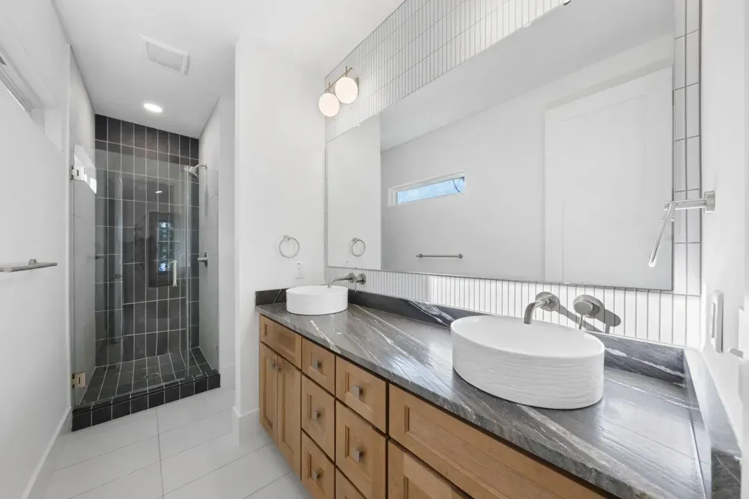 Modern bathroom with glass shower, wood vanity, and double sinks