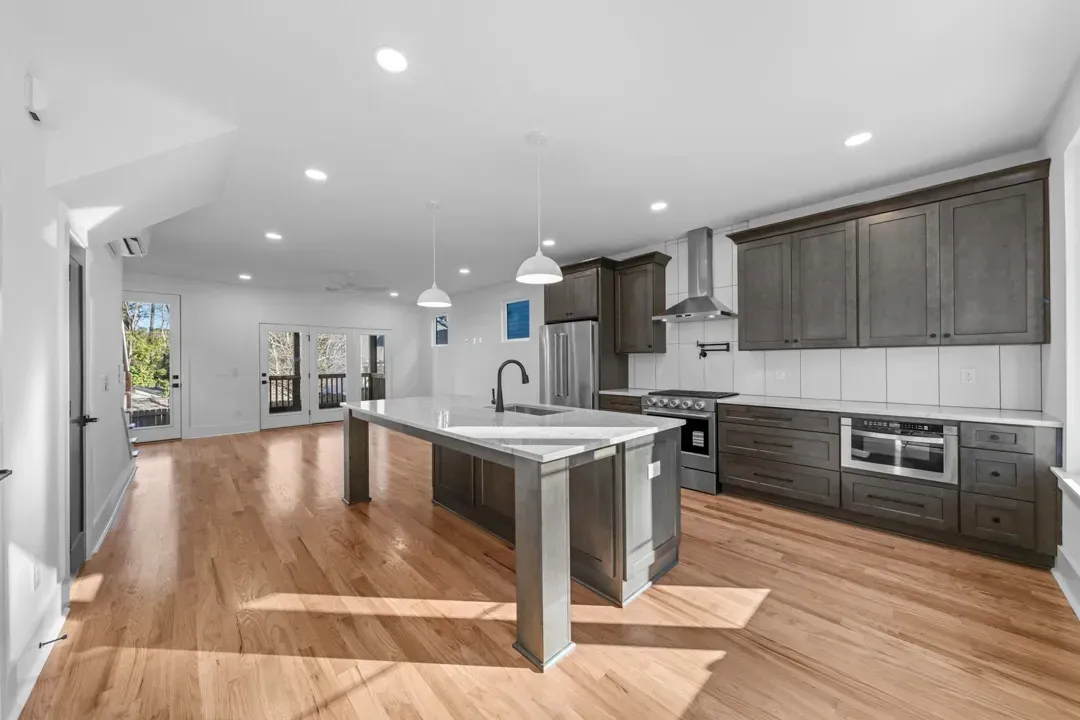 Bright modern kitchen with white island, gray cabinets, stainless appliances, and hardwood floors