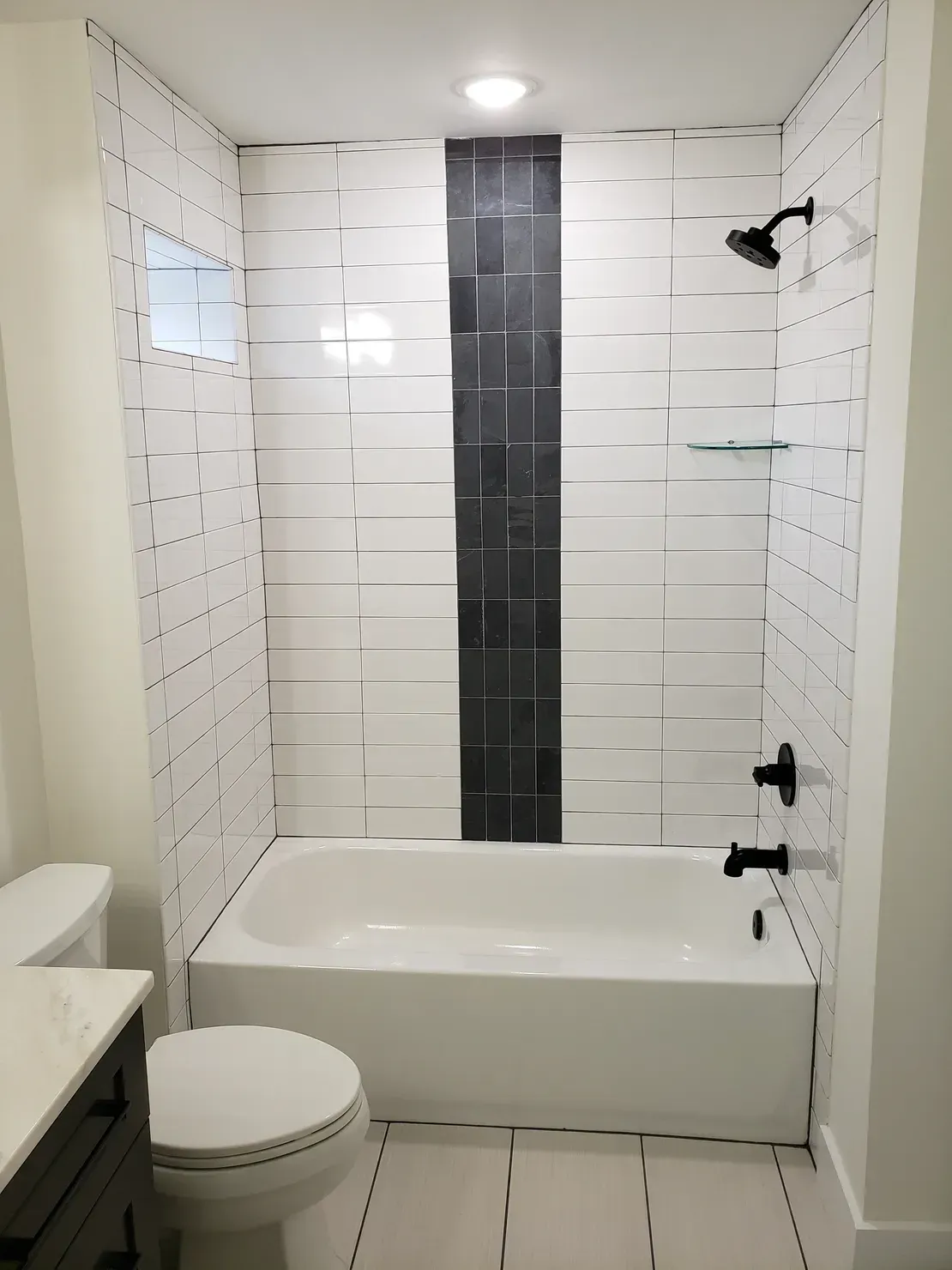 Small tiled bathroom with a bathtub, toilet, sink, and black fixtures.