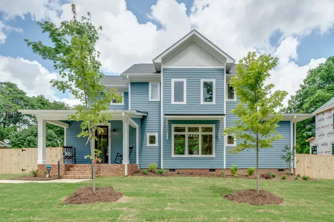 Blue two-story house with front porch, large windows, and young trees in a grassy yard