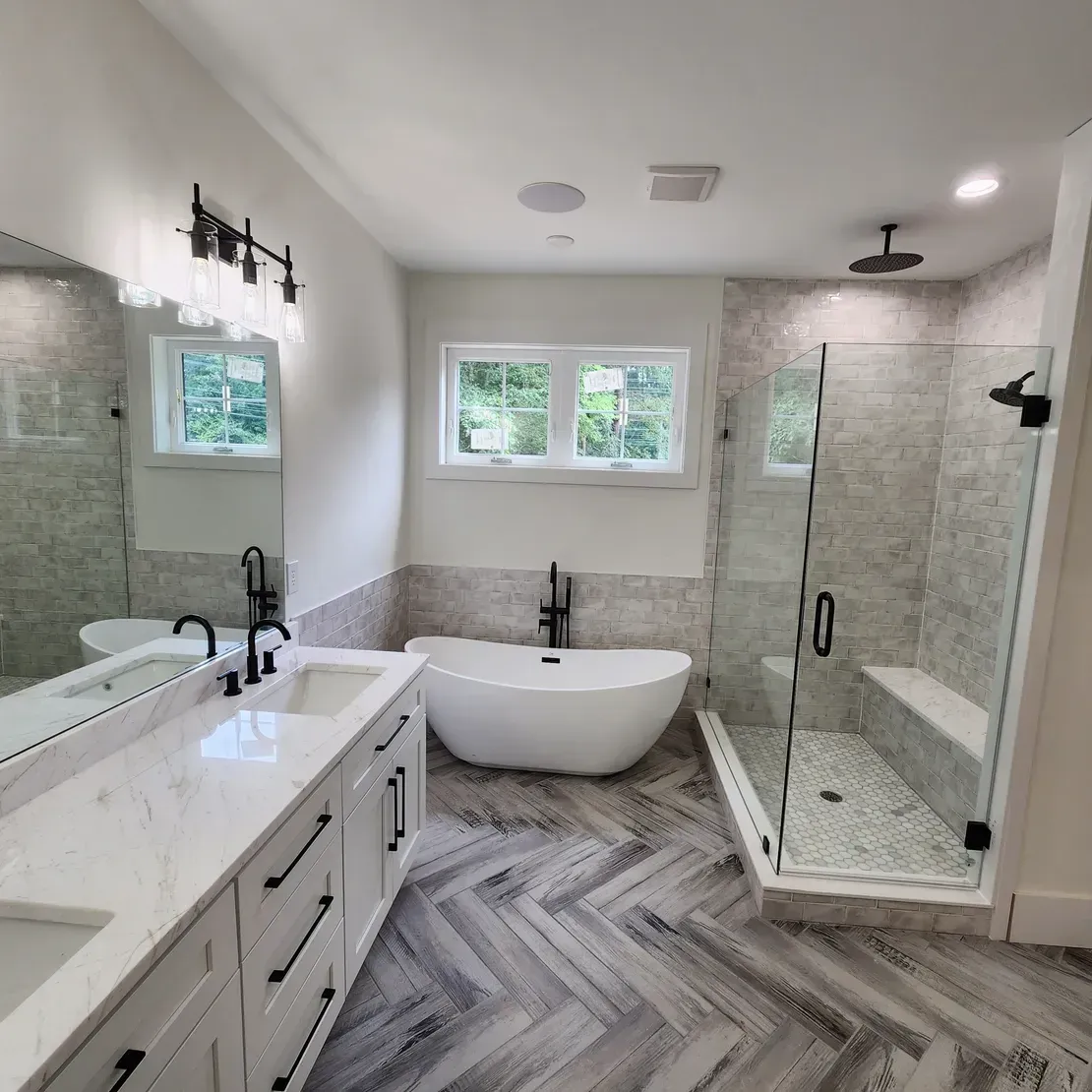 Bright modern bathroom with double vanity, freestanding tub, and glass shower in gray tile