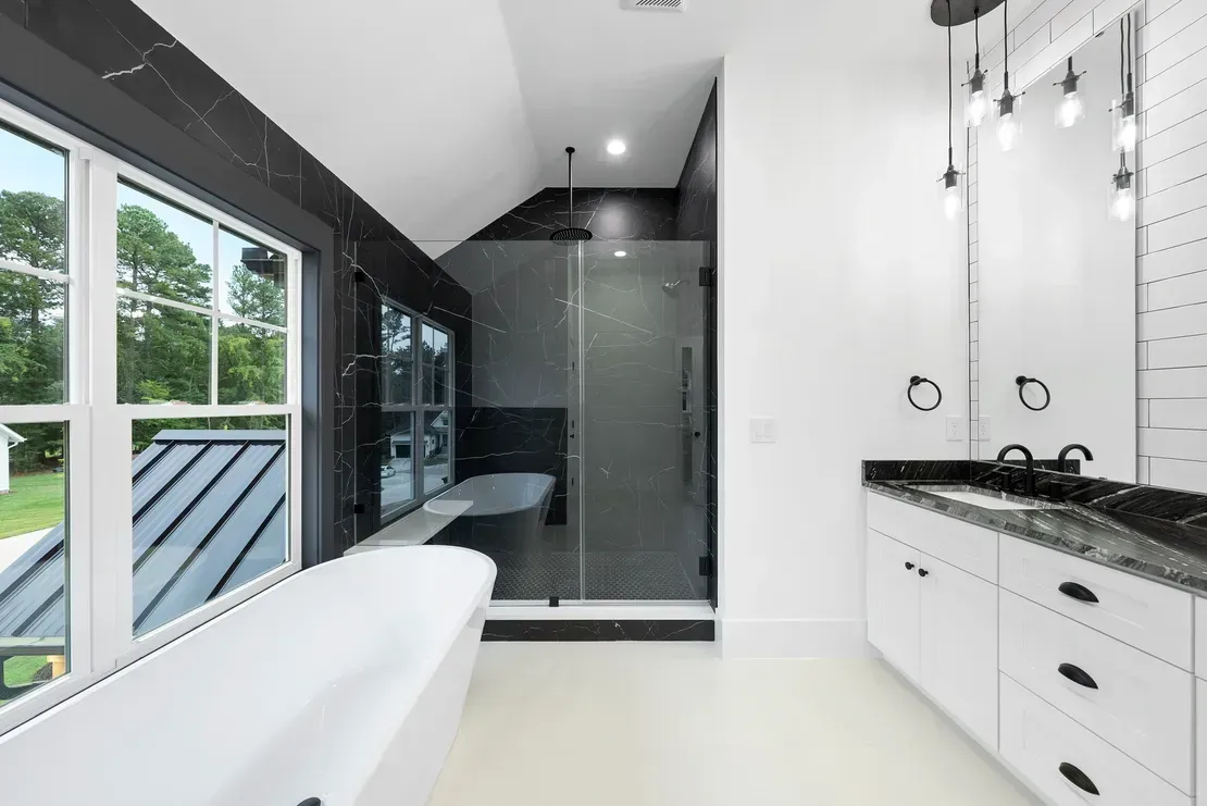 Modern bathroom with freestanding tub, black-tiled shower, and white vanity beside large windows