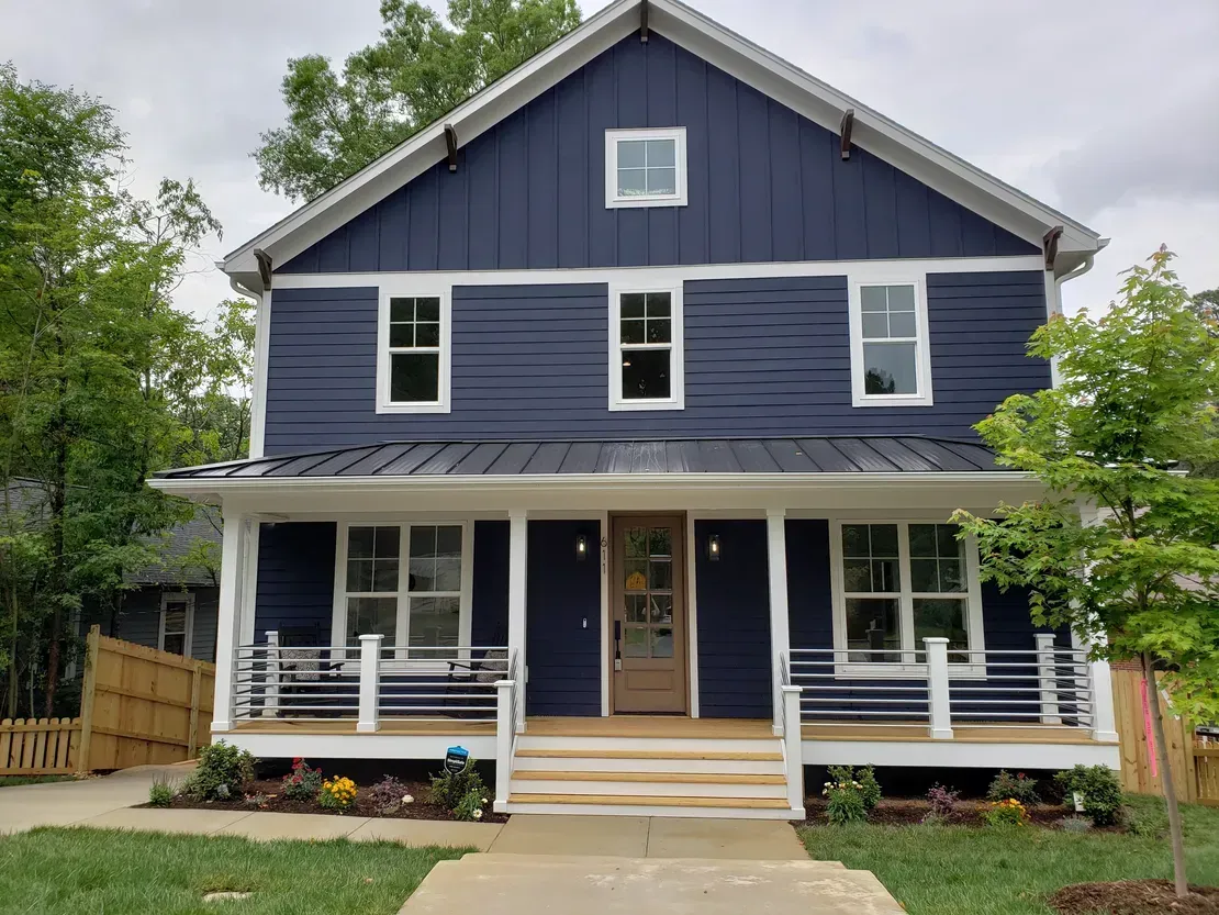 Blue two-story house with white trim and a front porch, centered in a leafy yard
