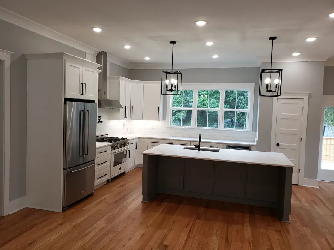 Modern white kitchen with island, stainless steel appliances, hardwood floors, and two pendant lights