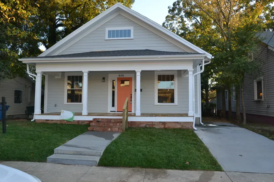 Small white house with a front porch, pink door, and concrete walkway leading to the entrance.