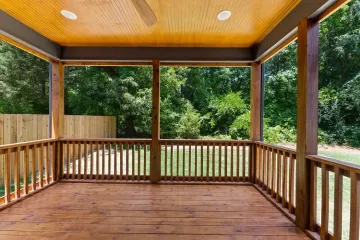 Covered wooden porch with railings and a view of green trees and lawn