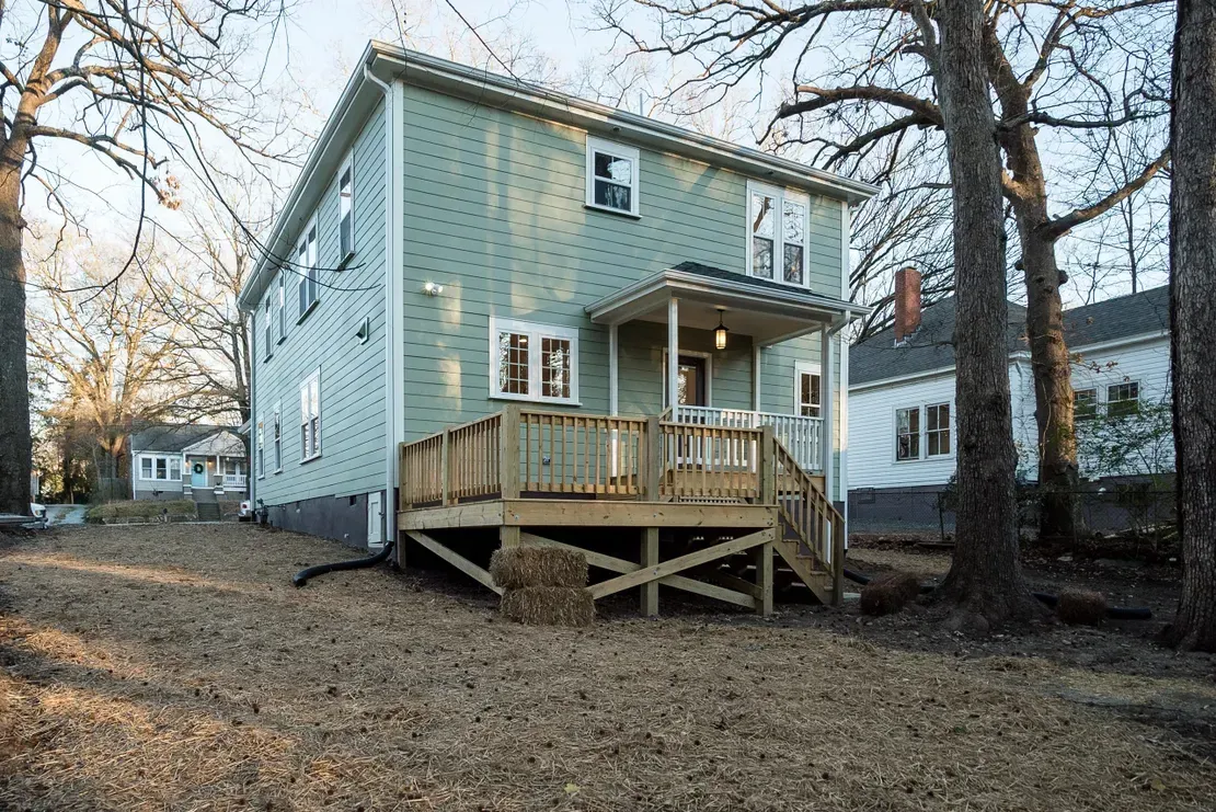 Light blue two-story house with a wooden porch in a wooded yard at dusk