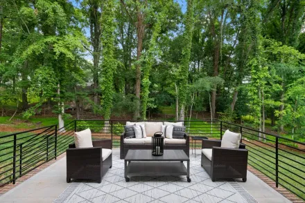 Patio seating area with black chairs and a table overlooking a lush green wooded backyard.