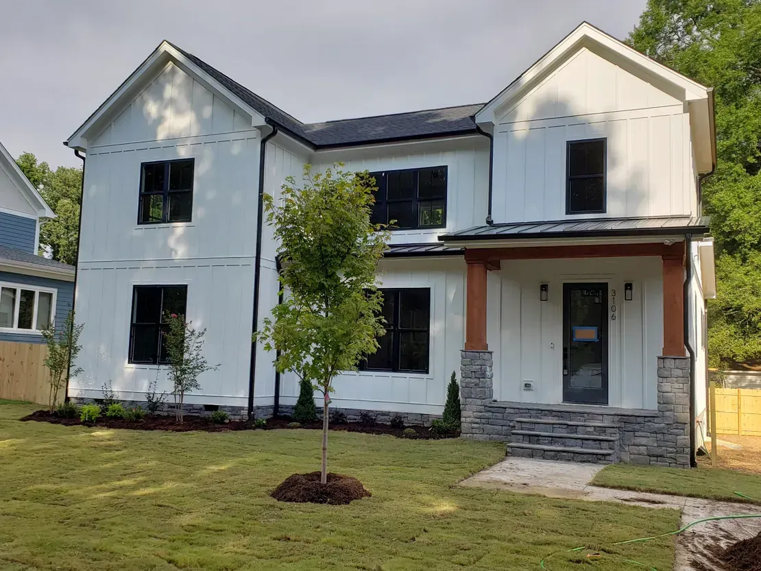 New white two-story house with black trim, front porch, and a small tree in the yard