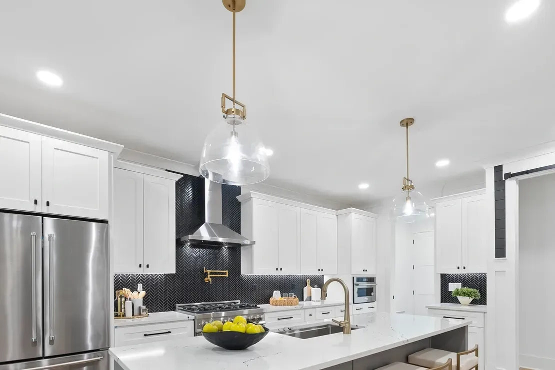 Bright white kitchen with stainless appliances, black backsplash, and a large island with fruit bowl