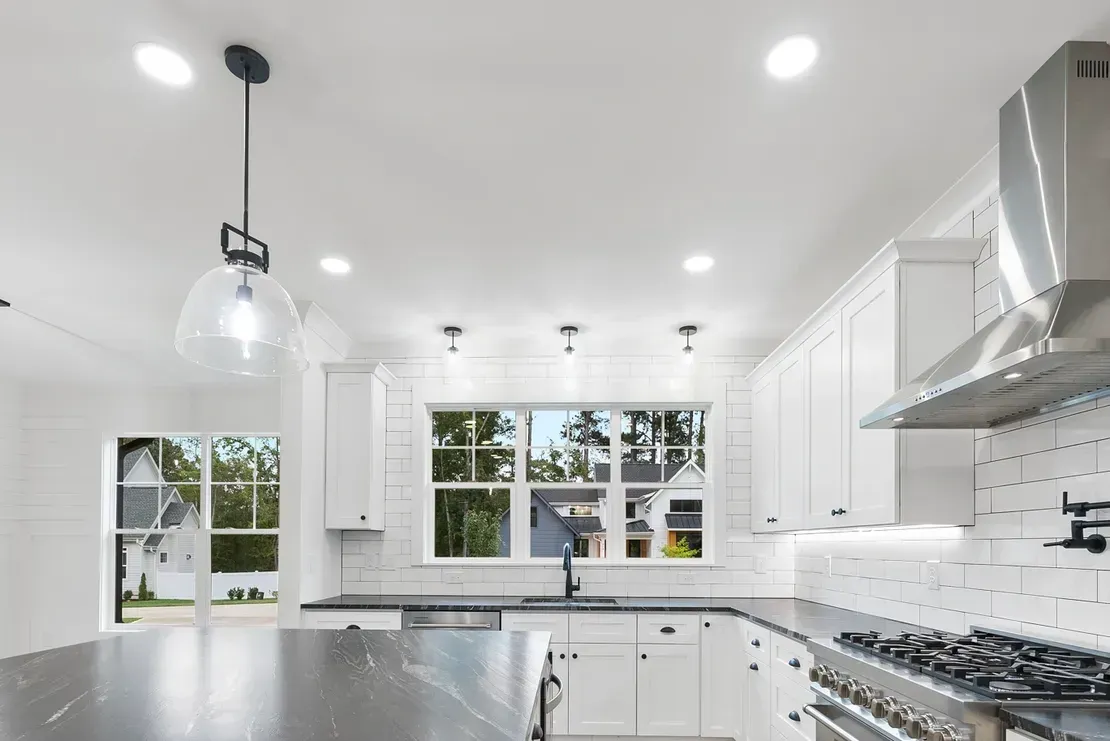 Bright white modern kitchen with black countertops, pendant lights, and stainless steel appliances