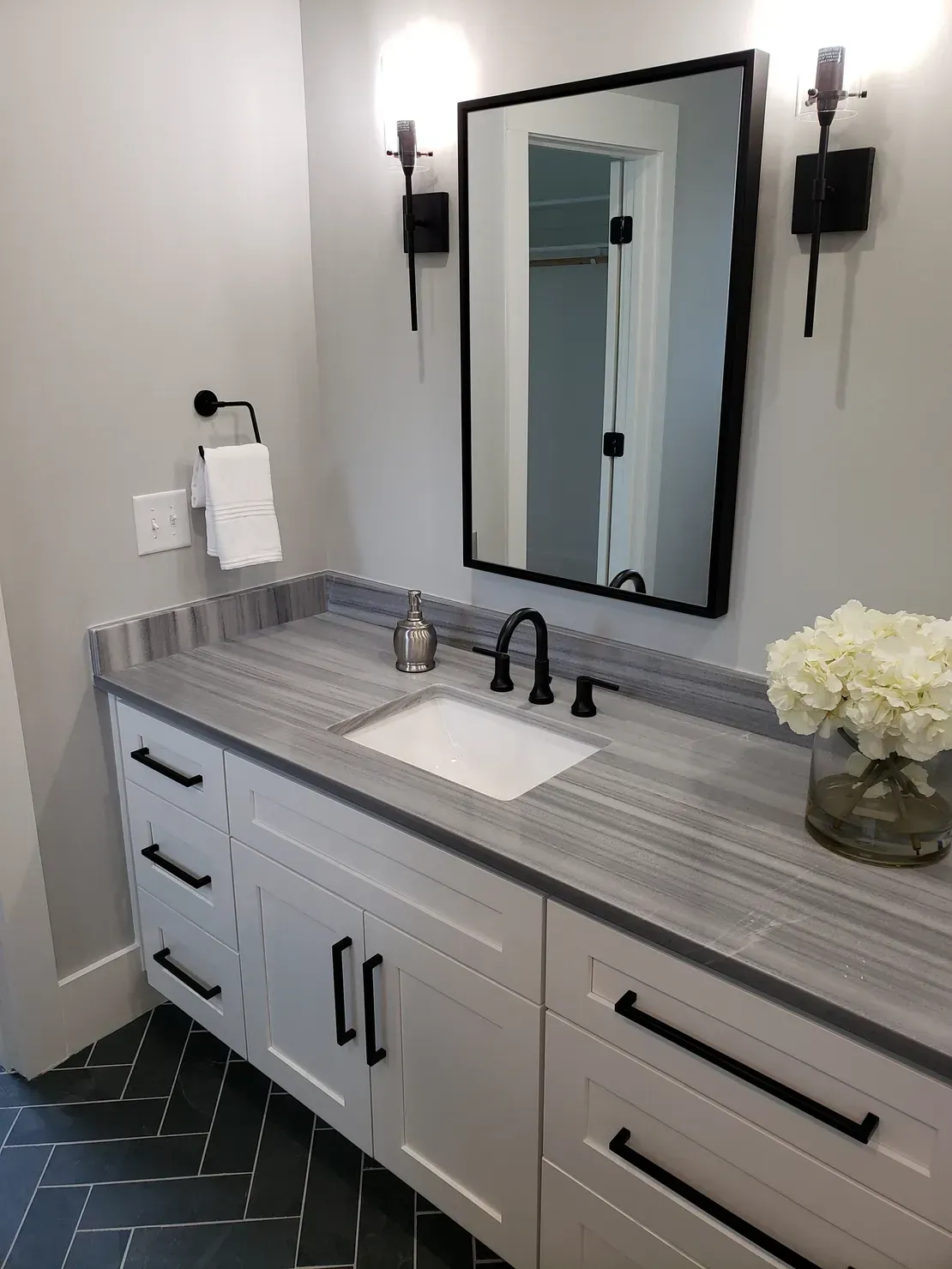 Modern bathroom vanity with gray cabinets, black mirror, wall sconces, and a white vessel sink