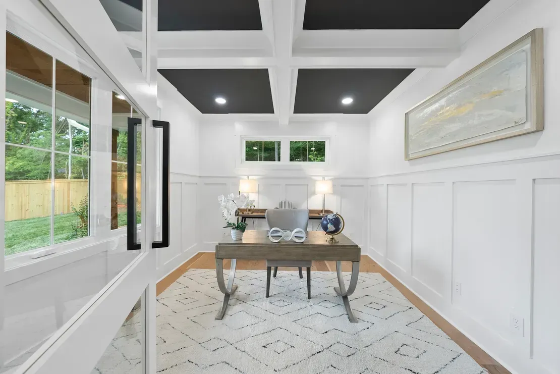Bright dining room with black ceiling panels, white wainscoting, and a wooden table on a patterned rug