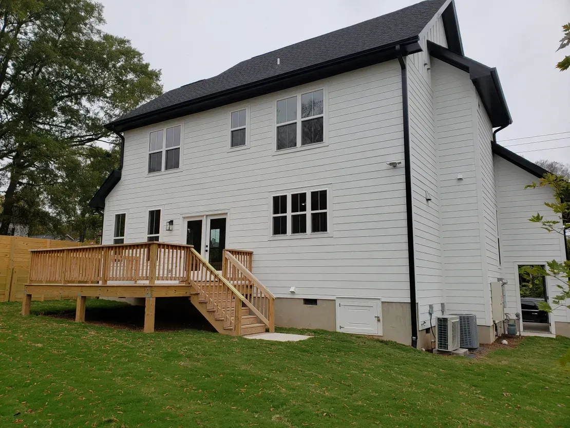 White house with dark roof and wooden deck on a grassy hillside, viewed from the side
