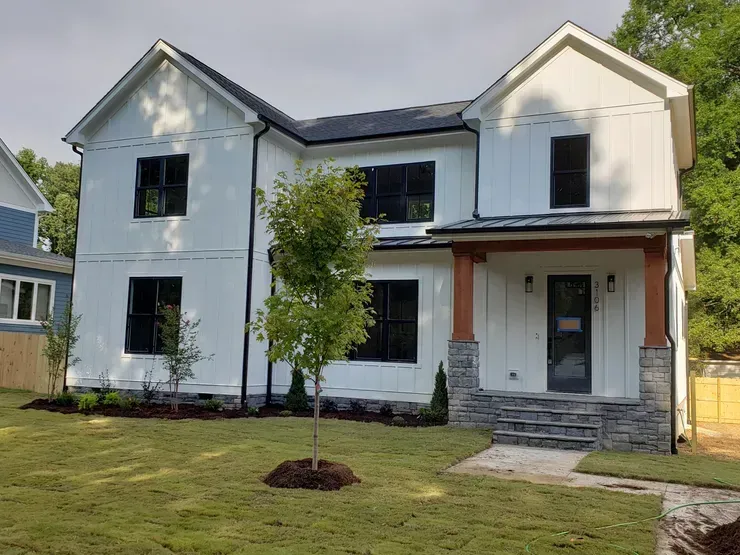 White two-story house with black-trimmed windows, front porch, and a young tree in the lawn