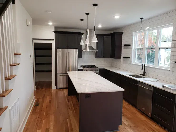 Modern kitchen with dark cabinets, stainless steel appliances, white island, and hardwood floors