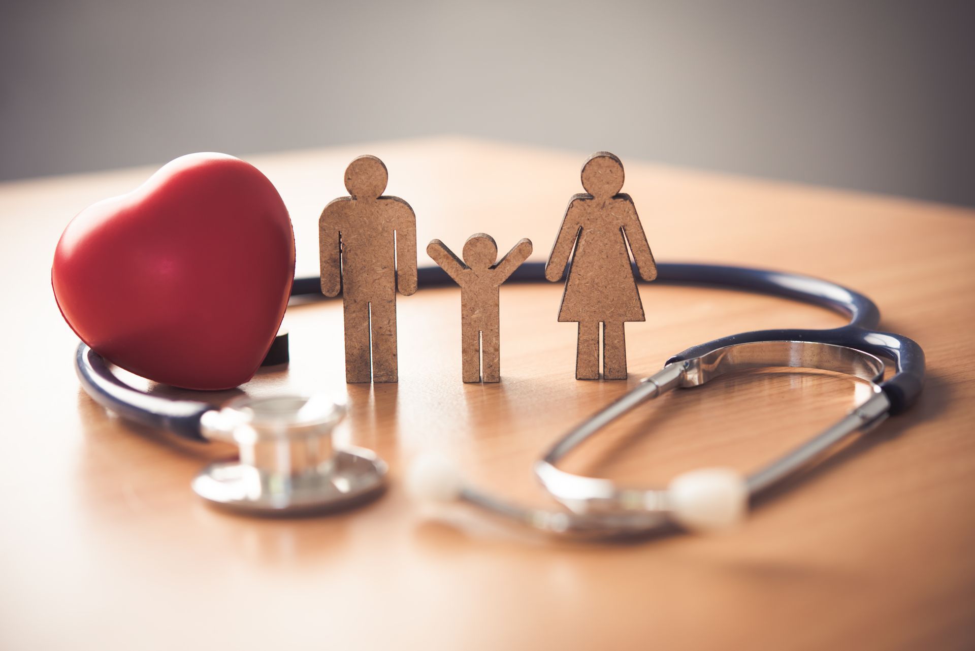 A red heart, family figurines, and stethoscope symbolizing healthcare and family well-being on a wooden table.