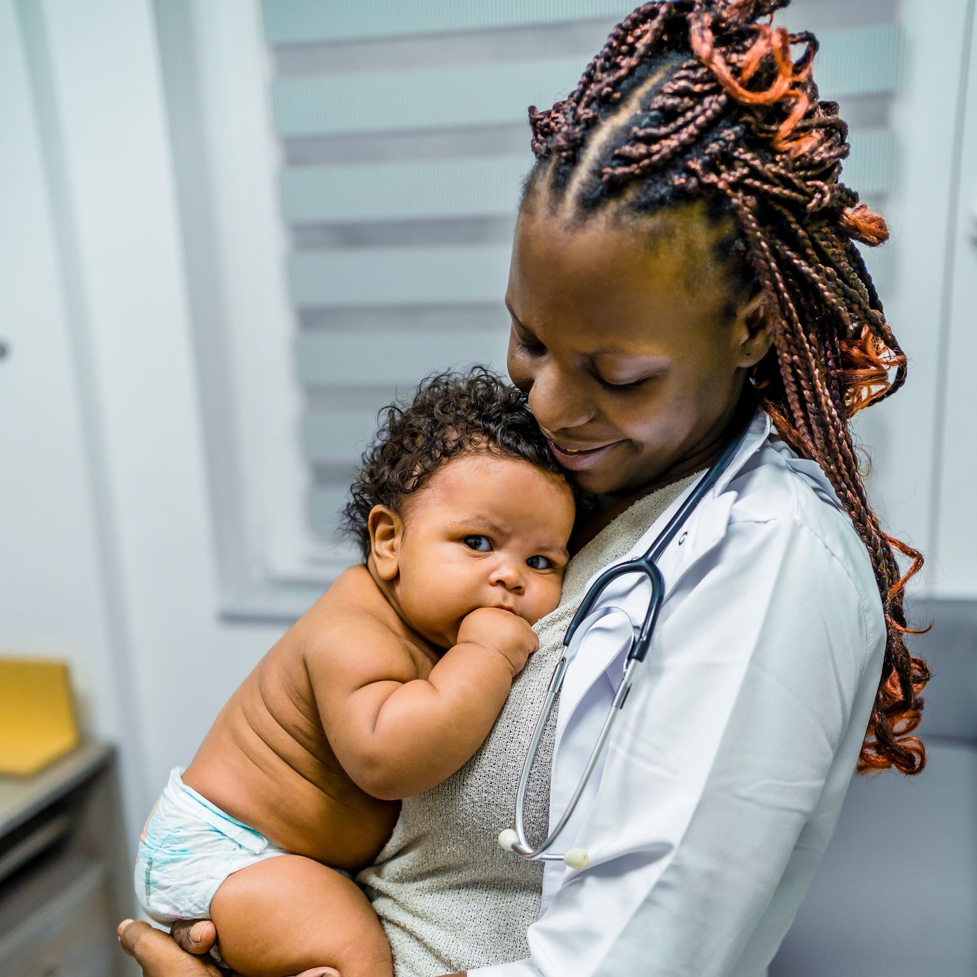 Doctor holding a baby in an exam room. The baby is wearing a diaper and looking at the camera.