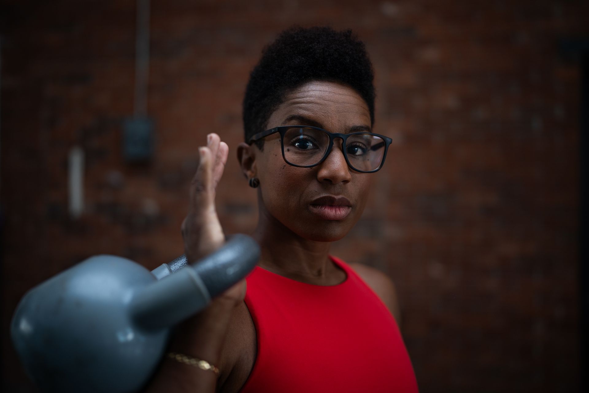Person in red shirt raising a hand toward a blurred gray object against a brick wall background