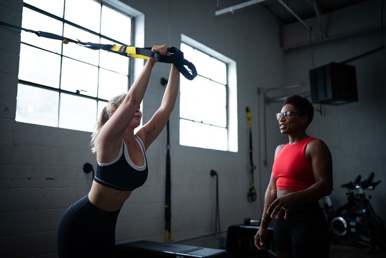 Woman exercising with suspension straps while a trainer watches in a gym