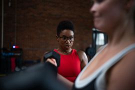 Gym scene with two people, one focused on a workout in a red top and the other blurred in the foreground