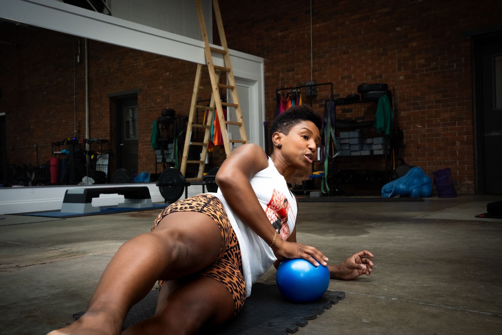 Person stretching on a blue ball in a garage, with a ladder and workout gear in the background.
