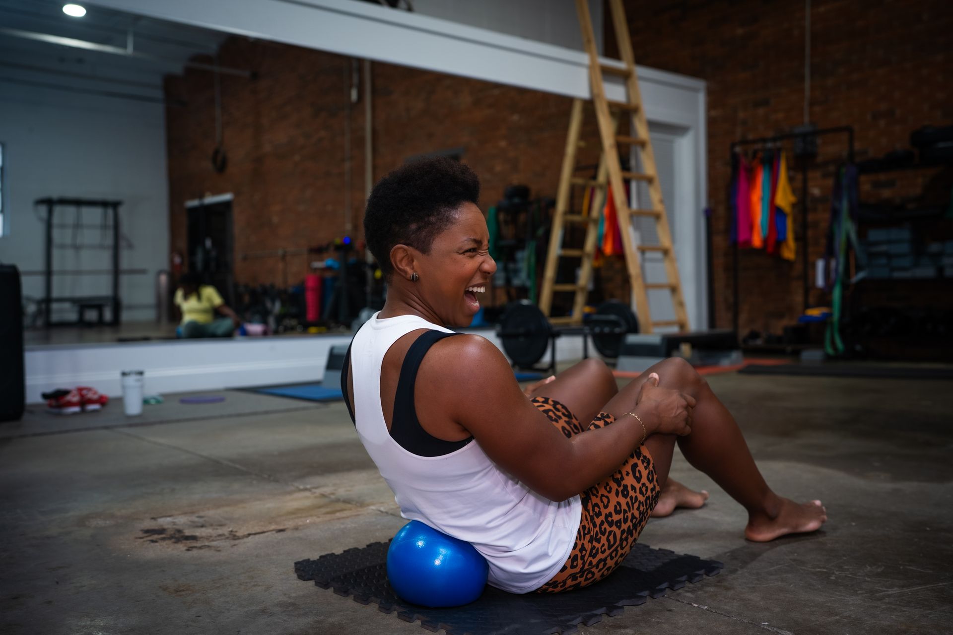 Person on a blue exercise ball in a gym, smiling and stretching on the floor.