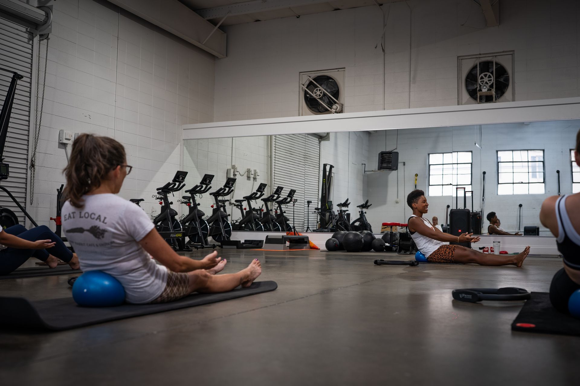 People doing seated yoga stretches in a bright studio with blue exercise balls and mats