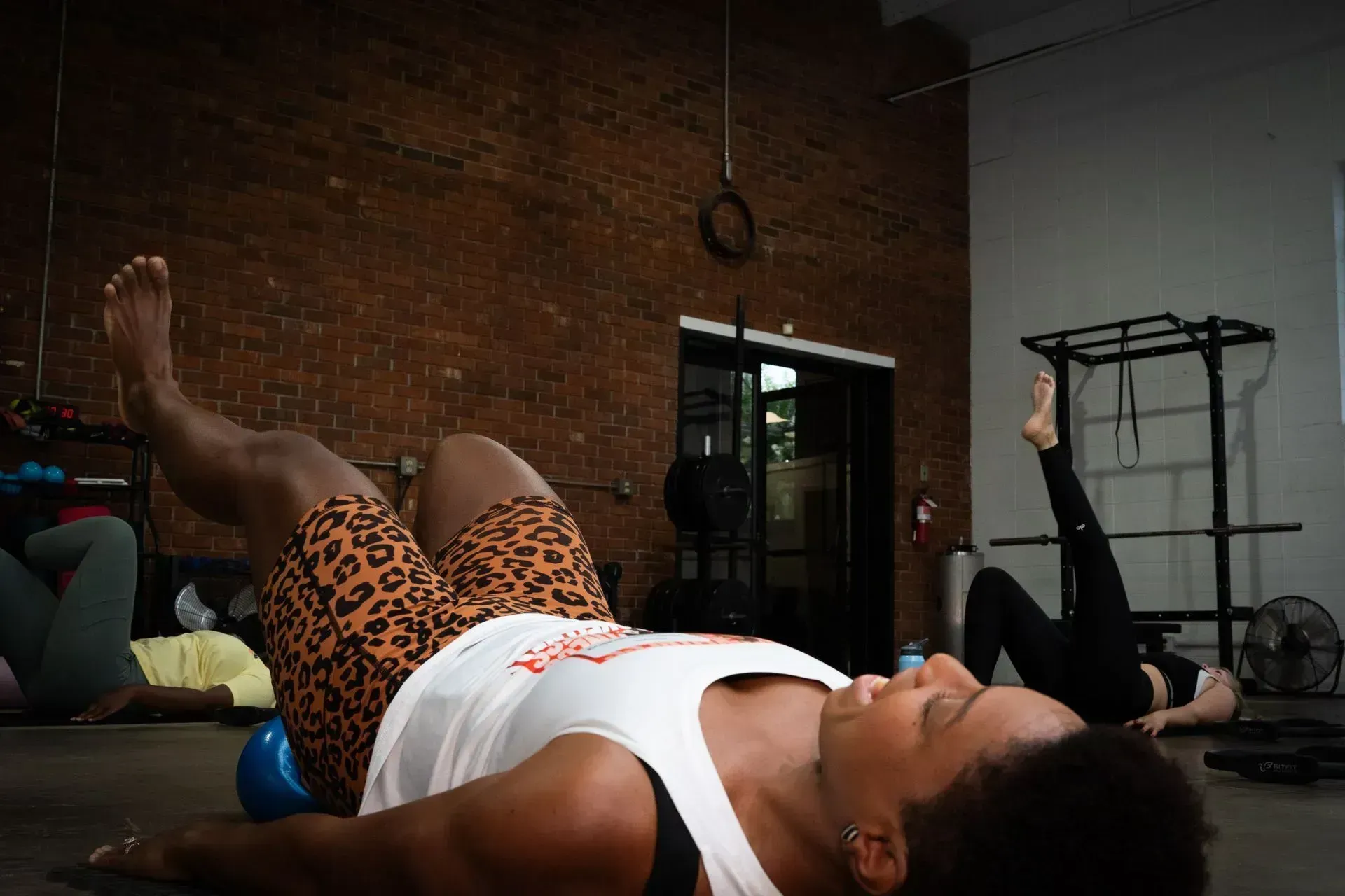 People doing floor exercises in a gym, one in the foreground with legs raised.