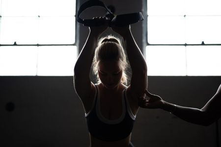 Silhouetted athlete lifting a kettlebell overhead in front of bright windows