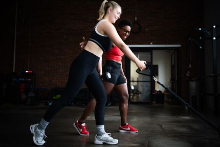 Two people doing battle rope exercises in a gym, one in black and white, the other in red and black.
