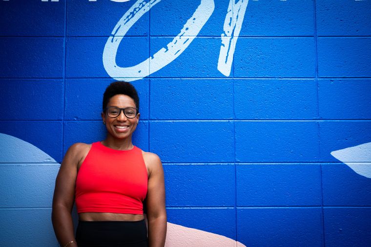 Smiling person in a red top standing against a bright blue mural wall
