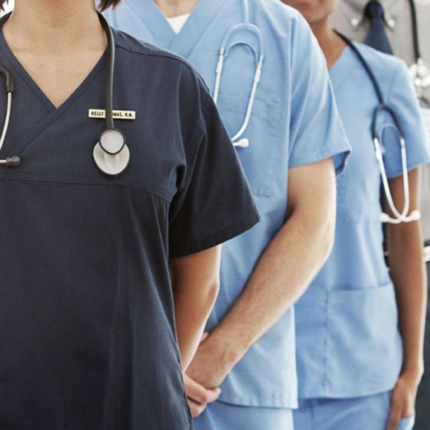 A woman in a purple scrub suit is standing with her hands in her pockets.