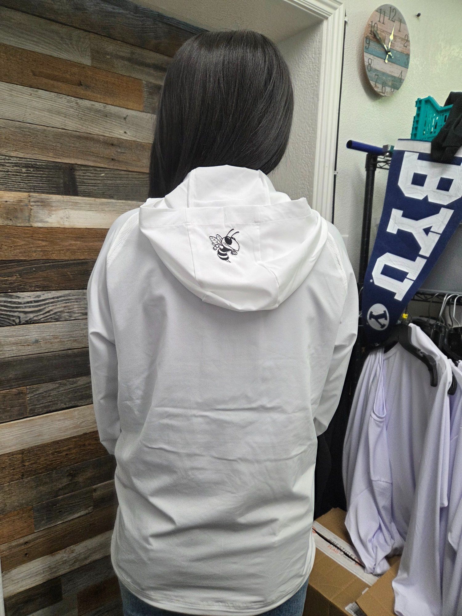 Person wearing a white hooded jacket, standing indoors. BYU banner visible.