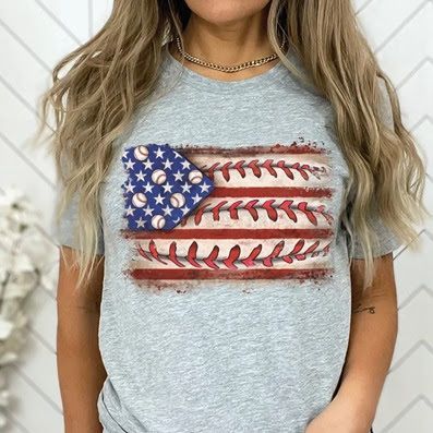 A woman is wearing a gray t-shirt with an american flag and baseballs on it.