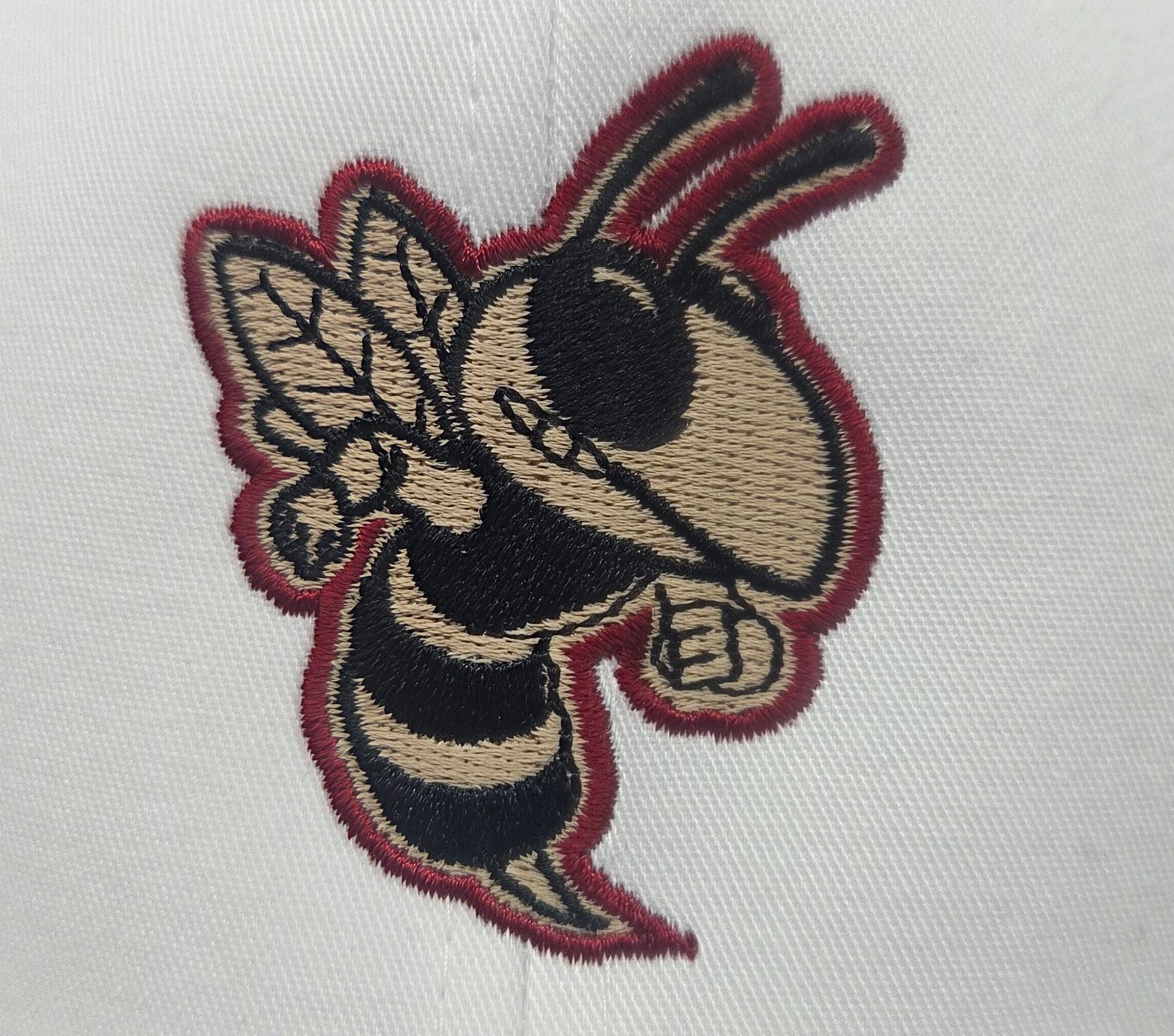 Embroidered cartoon wasp logo, red outline, beige wings and head, black and beige body, angry expression.