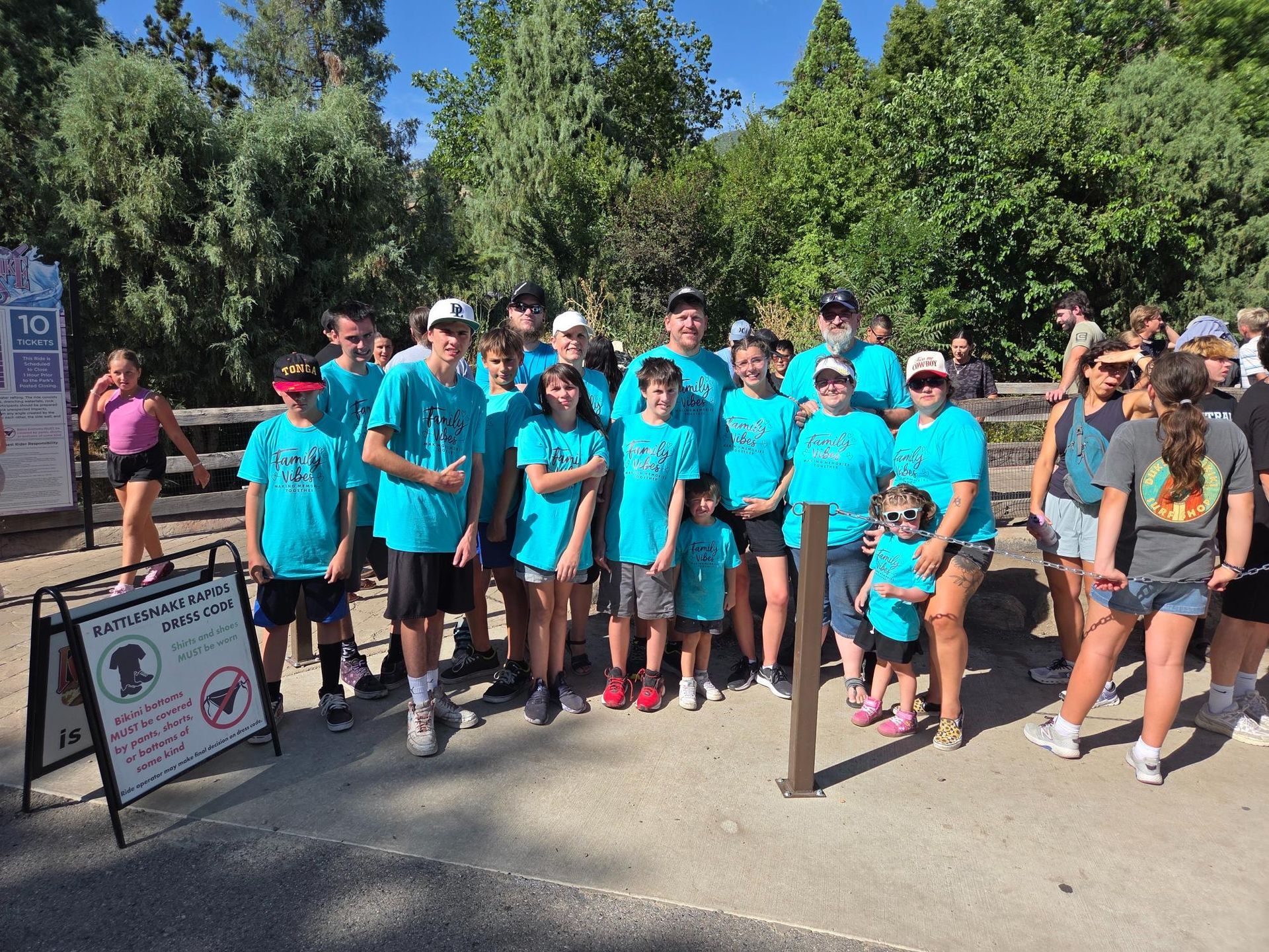 Group of people in teal shirts standing outdoors, posing for a photo near a sign and a wooden fence.
