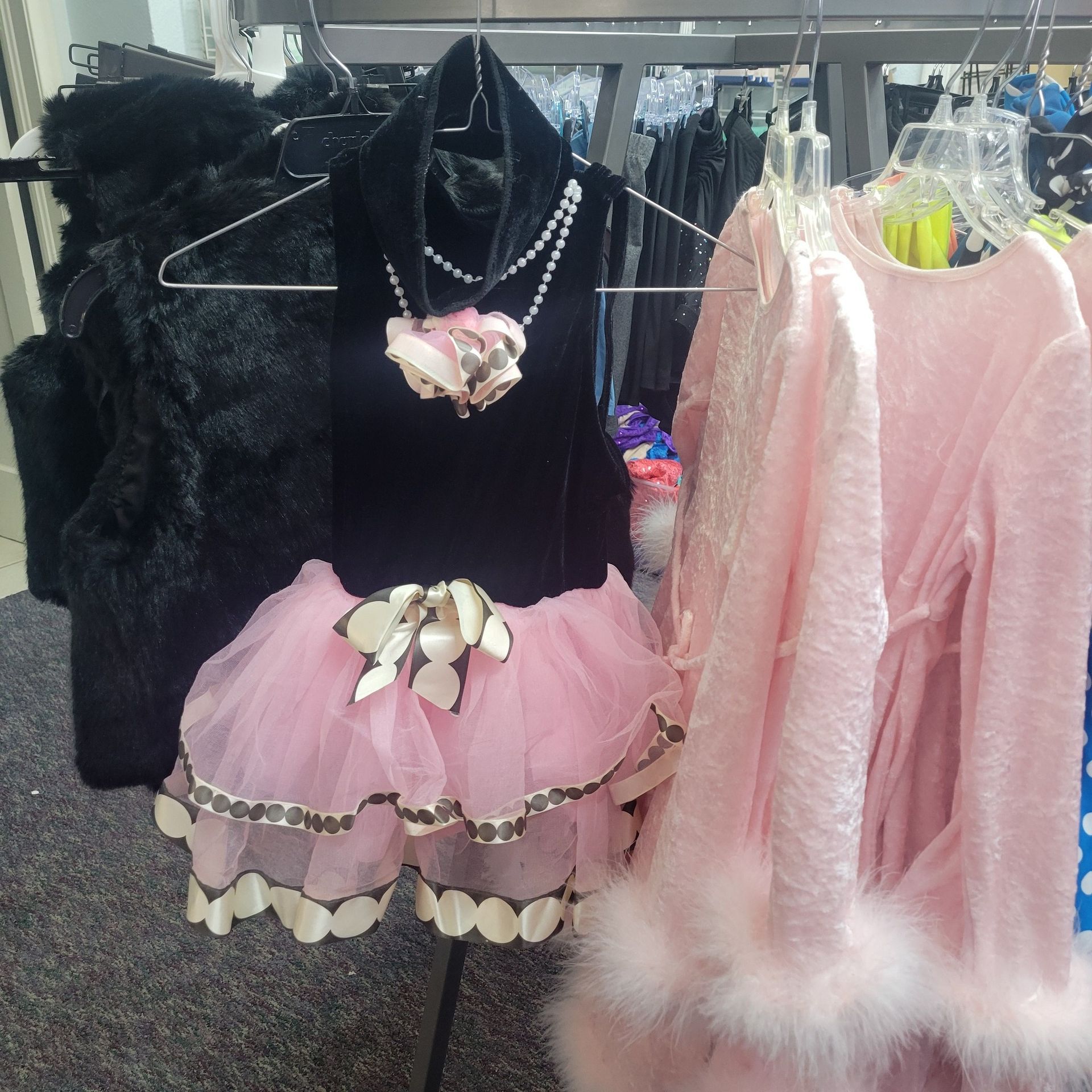 A black fur vest and a pink dress are hanging on a rack