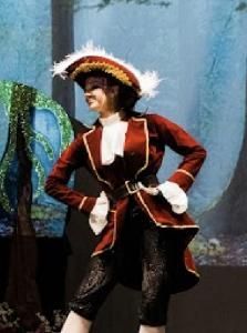 Person in a red pirate costume with a feathered hat, posing with hands on hips before a painted forest backdrop