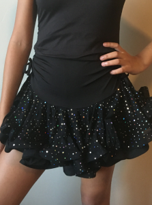 Black dress with sequined ruffled skirt, model posing with hand on hip against a plain wall.