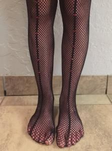 Lower legs and feet in black fishnet tights standing on a tiled floor.