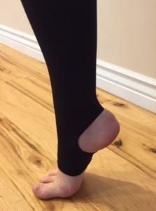Person standing on tiptoes indoors, wearing black leggings with one heel raised