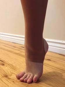Close-up of a bare foot and lower leg standing on a hardwood floor near a white baseboard.
