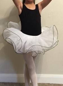Ballerina in black leotard and white tutu posing on tiptoe indoors against a plain wall