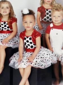 Four children in matching red-and-white polka dot outfits seated together against a plain background