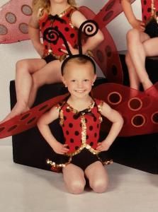 Child in a red-and-black ladybug costume posing onstage with other performers in the background